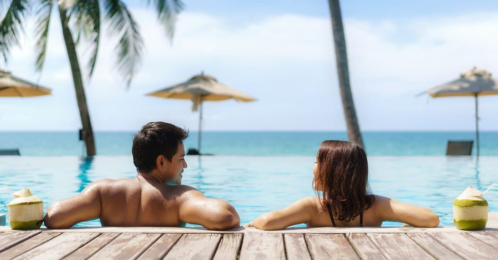 Couple relaxing in an infinity pool overlooking the turquoise Andaman Sea at a beachfront Khao Lak resort in Thailand.